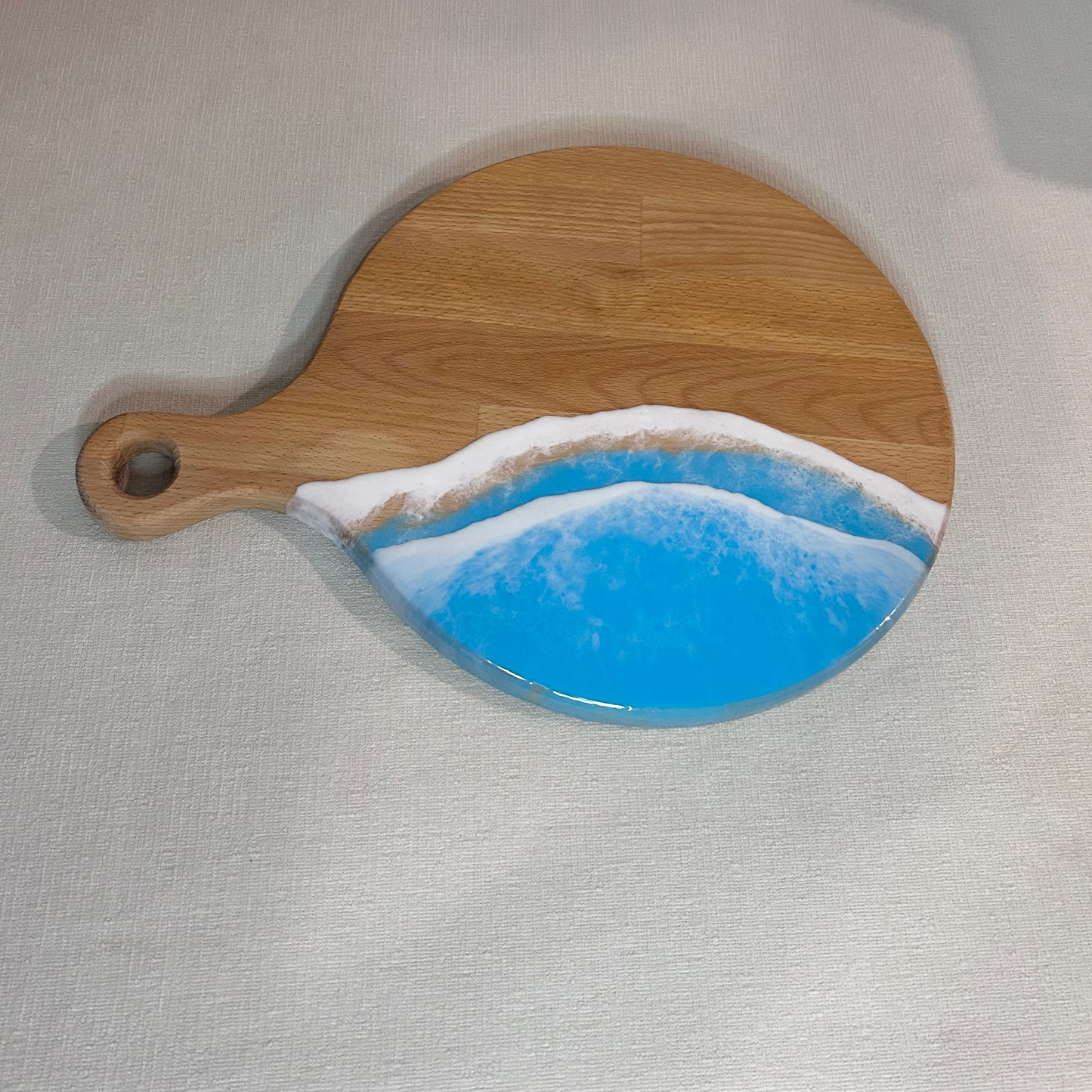 Platou / tocator rotund cu maner din lemn de fag cu rasina epoxidica, efect ocean albastru deschis. Personalizata cu un mesaj ales de tine - epoxyarta.ro